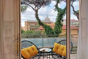 A balcony with two black wicker chairs, each with a yellow cushion, and a small round table with two wine glasses and a book.