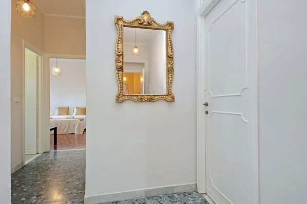 A hallway with a marble floor, a large ornate mirror, and a white door with a handle.