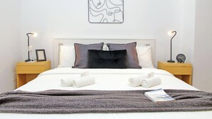 A neatly made bed with a dark throw blanket, two bedside tables with lamps, and a wall art piece above the bed.