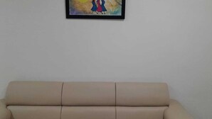Beigenvärinen sohva on sijoitettu pelkän seinän eteen, ja sen yläpuolella on kehystetty taulu.