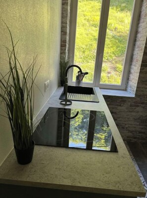 A kitchen with a black induction cooktop, a sink, and a window overlooking a garden. - Romantic cocoon Jardin de la Princesse ideal couple, Calm & Nature Vosges (Senones)