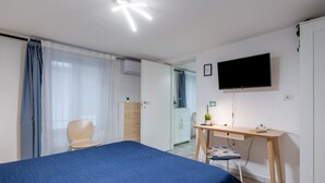 A bedroom with a bed, a desk, a chair, a TV, and a wardrobe. - GuestHost - Central apartment Caronda Compact (Catania)
