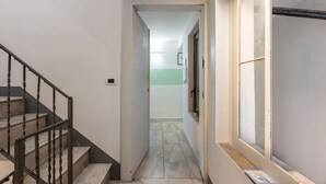 A narrow hallway with a staircase on the left, a window on the right, and a door at the end. - GuestHost - Central apartment Caronda Compact (Catania)