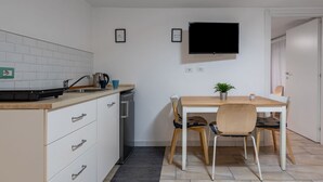 A compact kitchen with a dining area, a flat-screen TV mounted above the table, and a small potted plant on the table. - GuestHost - Central apartment Caronda Compact (Catania)