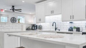 Una cocina moderna con armarios blancos, una isla grande y un ventilador de techo.