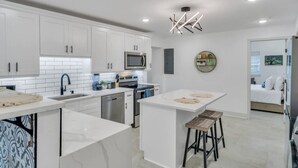 Una cocina moderna con armarios blancos, una isla central y una zona de comedor con taburetes.