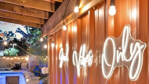 Un mur en bois orné d’enseignes au néon qui forment les mots « Good Vibes Only », et un espace piscine illuminé de guirlandes lumineuses.