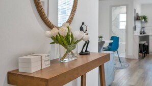 Une console en bois ornée d’un vase de fleurs blanches, d’une petite sculpture et d’une plaque portant l’inscription « chez soi, on est bien », le tout dans un intérieur moderne.