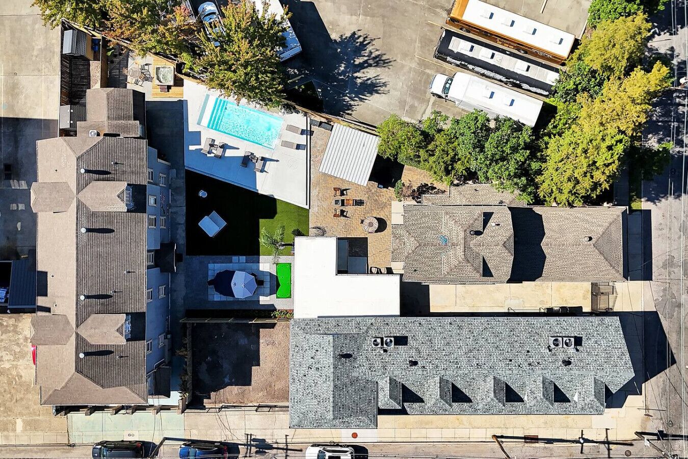 An aerial view of a residential area with multiple buildings, including a house with a swimming pool, a garage, and a small garden.