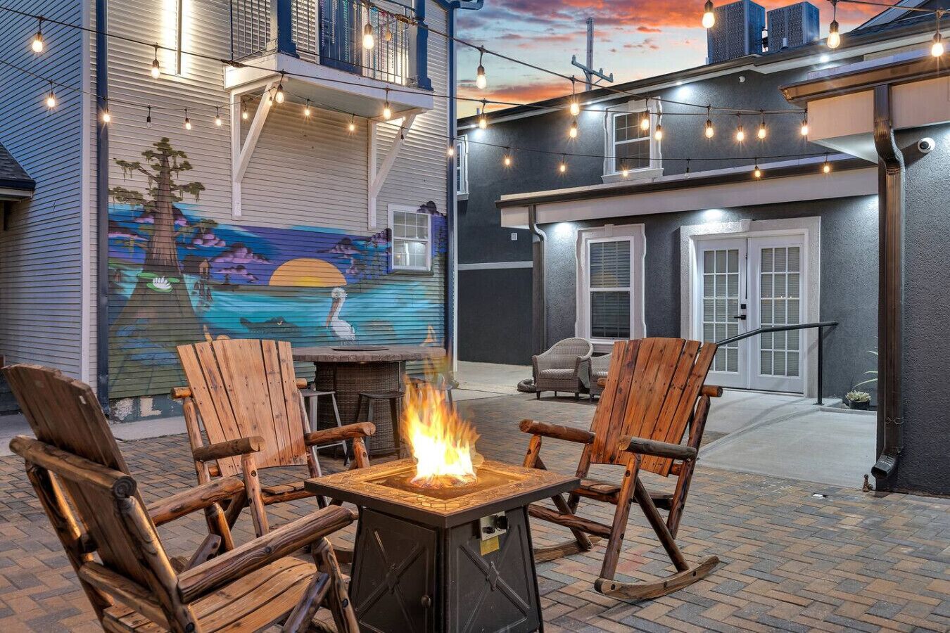 An outdoor patio with a fire pit, wooden chairs, and string lights.