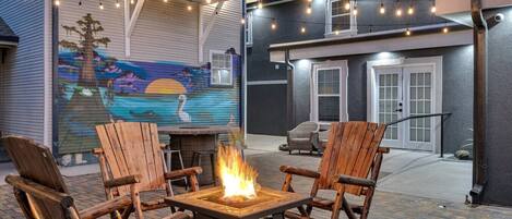 An outdoor patio with a fire pit, wooden chairs, and string lights.