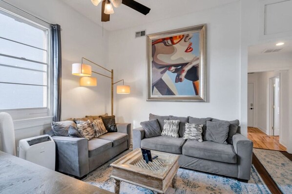 A modern living room with two grey sofas, a coffee table, and a painting on the wall.