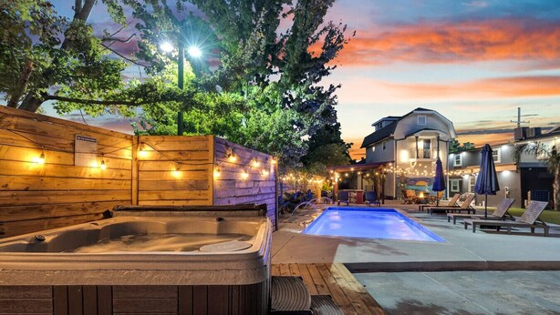 A hot tub and a pool area with lounge chairs and umbrellas, surrounded by wooden fences and string lights. - NOLA 3BR Escape w Pool, Steps from Canal Streetcar (New Orleans)