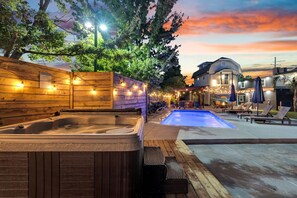 A hot tub and a pool area with lounge chairs and umbrellas, surrounded by wooden fences and string lights.
