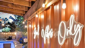 A wooden wall with neon signs spelling "Good Vibes Only" and a pool area with string lights. - NOLA 3BR Escape w Pool, Steps from Canal Streetcar (New Orleans)