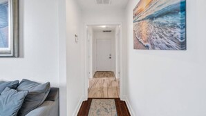 A hallway with a wooden floor, a door at the end, and a painting on the wall. - NOLA 3BR Escape w Pool, Steps from Canal Streetcar (New Orleans)