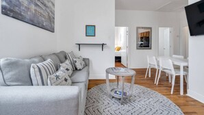 Un salon moderne avec un canapé gris, une table basse ronde et un téléviseur à écran plat fixé au mur.
