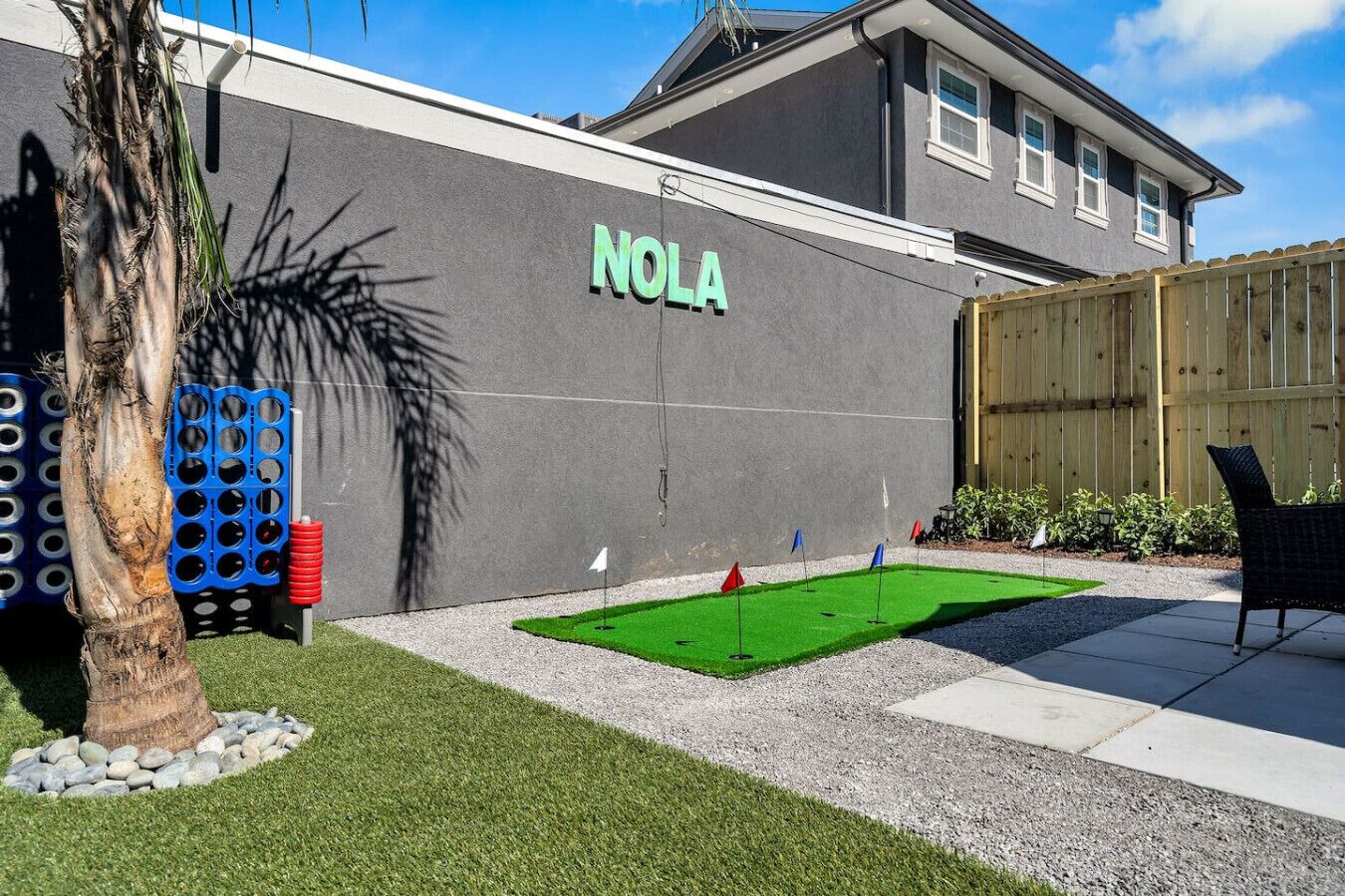 Um imóvel residencial com uma placa na parede com o nome 'NOLA', um pequeno gramado artificial verde e uma cerca de madeira.