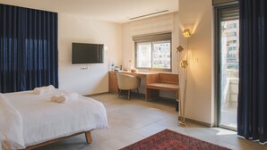 Ein Hotelzimmer mit Bett, Schreibtisch, Stuhl, Fernseher und einem Fenster mit Blick auf Gebäude.