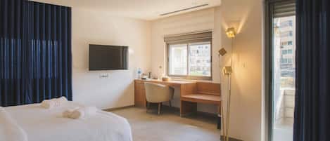 Hotellihuone, jossa on sänky, työpöytä, tuoli, televisio ja ikkuna, josta on näkymä rakennuksiin.