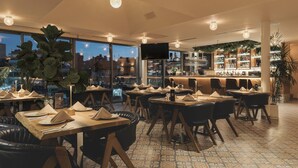 Ein Restaurant mit gedeckten Tischen, einer Bar mit Flaschenregalen und großen Fenstern mit Blick auf die Stadtlandschaft.
