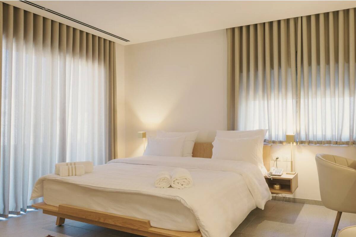 Habitación de hotel moderna con una cama grande, dos mesitas de noche, una silla y un escritorio.