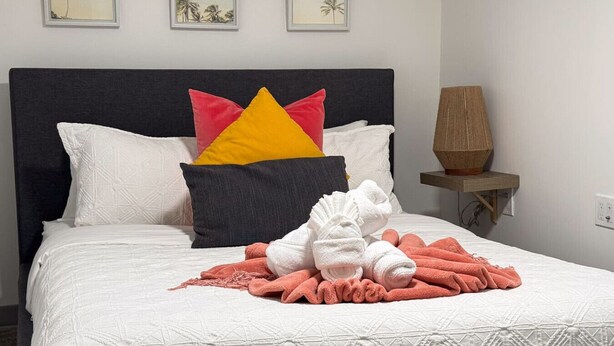 Ein ordentlich bezogenes Bett mit weißer Decke, verschiedenen Kissen und einer Reihe Handtücher.