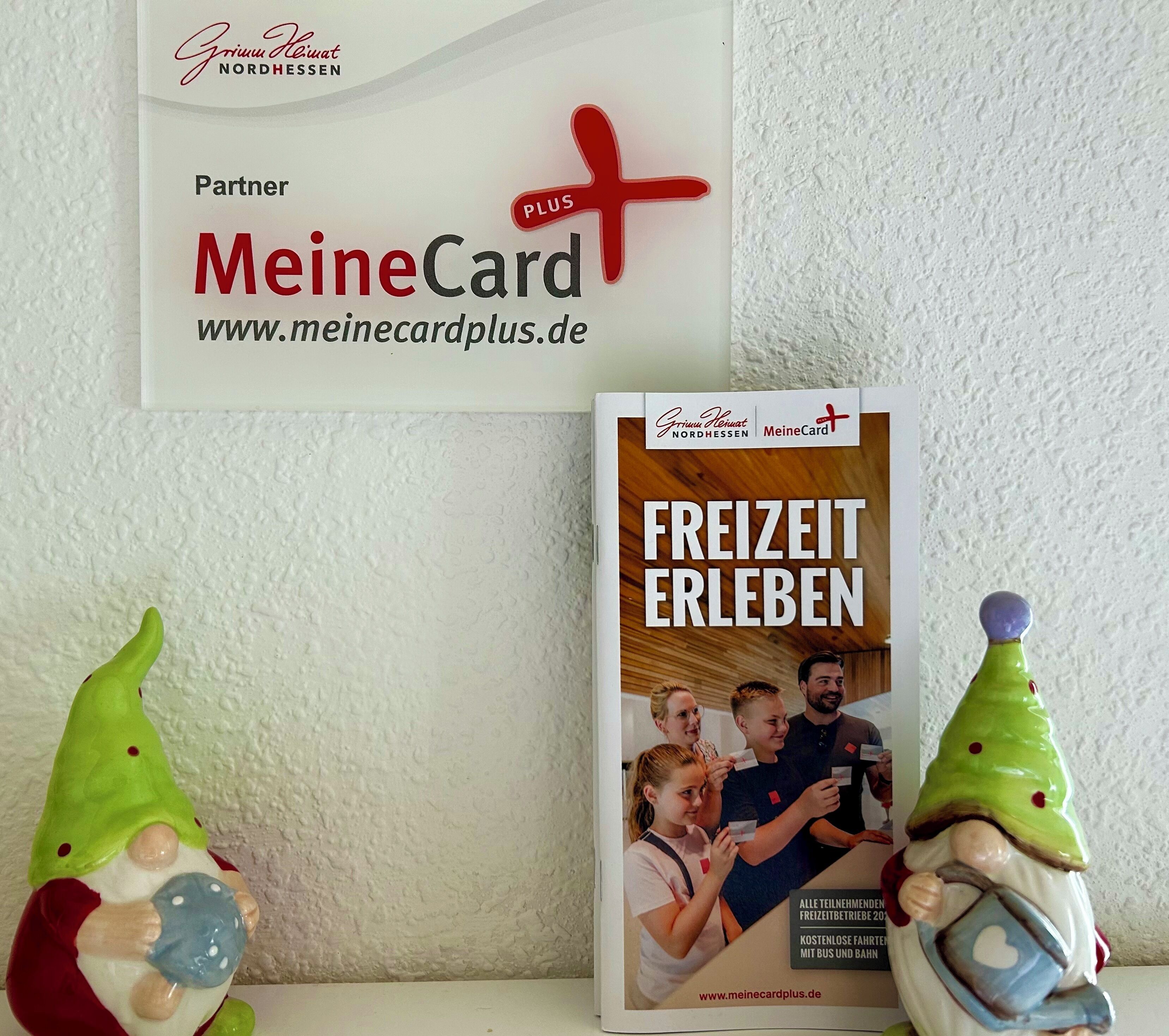 A promotional card for MeineCard PLUS and a brochure titled 'FREIZIT ERLEBEN' with a gnome figurine.