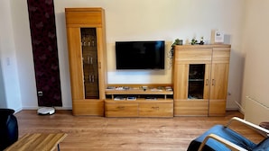 Moderni olohuone, jossa on puinen kaappi, litteänäyttöinen televisio ja sohva.