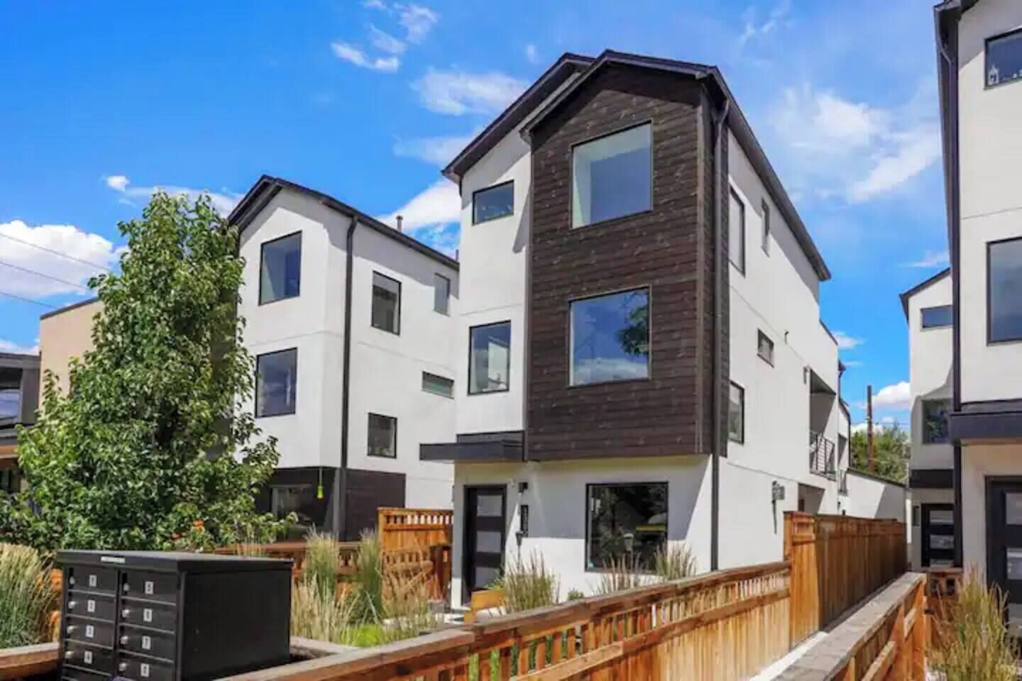 A modern multi-story residential building with a flat roof, large windows, and a wooden deck in front.