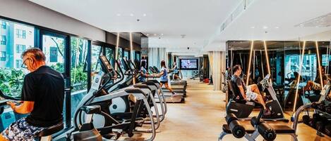 Une salle de sport moderne équipée de tapis de course, de vélos elliptiques et d’appareils de musculation.