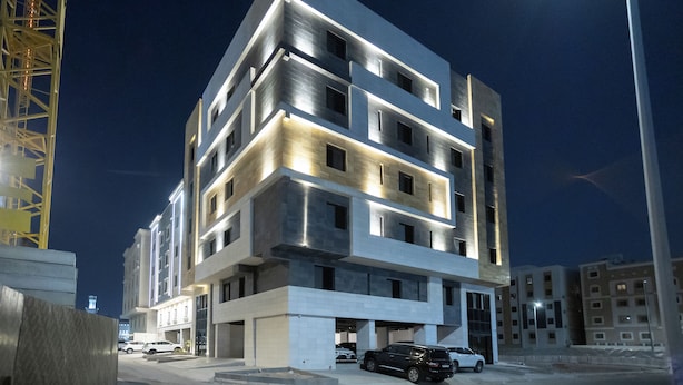 A modern multi-story building with a flat roof, large windows, and a parking area with several cars. - Manazel Marez 2 - private apartments (Madinah)