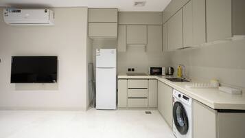 A modern kitchen with a built-in washer and dryer, a flat-screen TV, and a refrigerator.