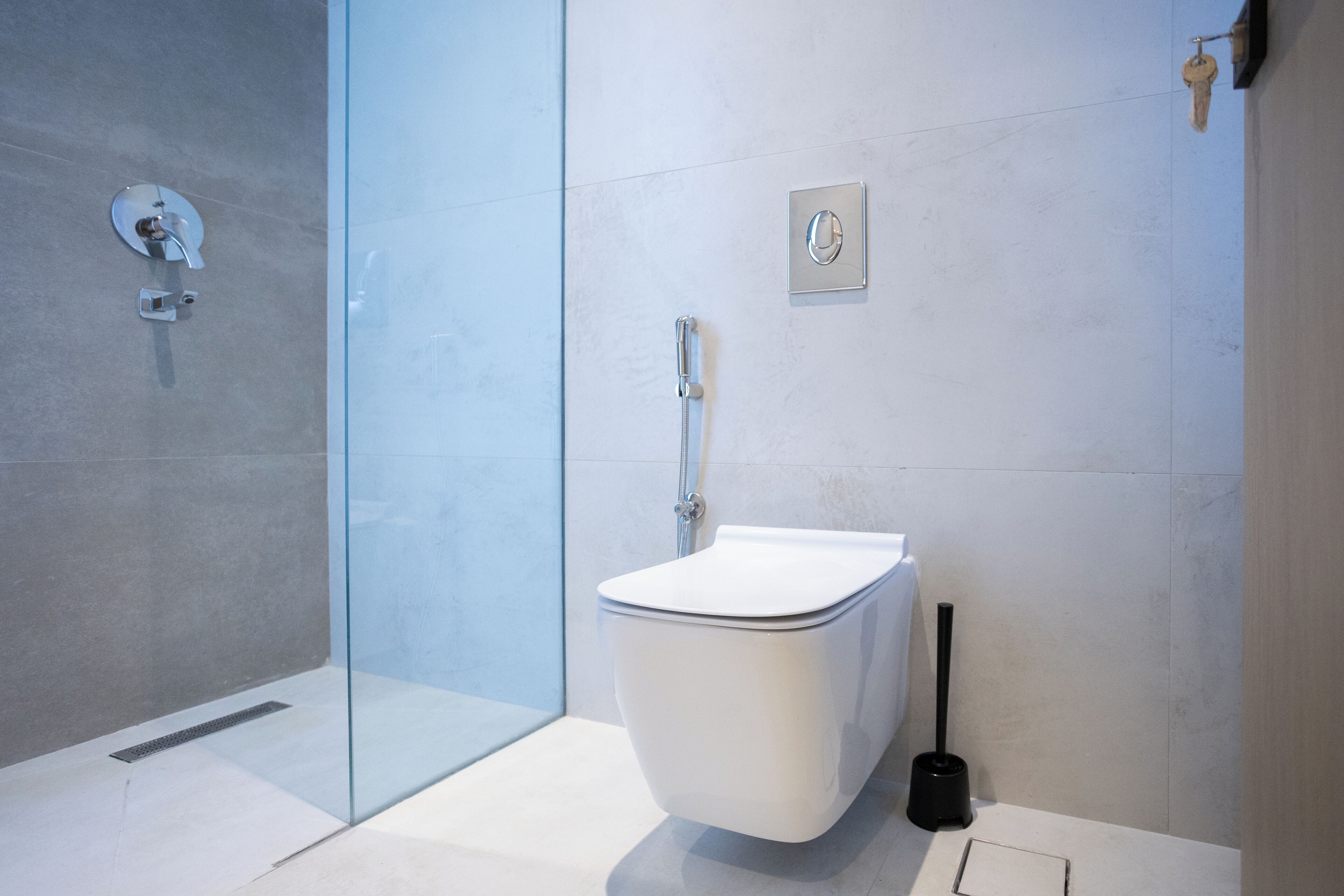 Un baño moderno con cabina de ducha de vidrio, inodoro blanco y escobilla de inodoro negra.