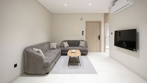 A modern living room with a grey sofa, a wooden coffee table, and a flat-screen TV mounted on the wall. - Manazel Marez 2 - private apartments (Madinah)