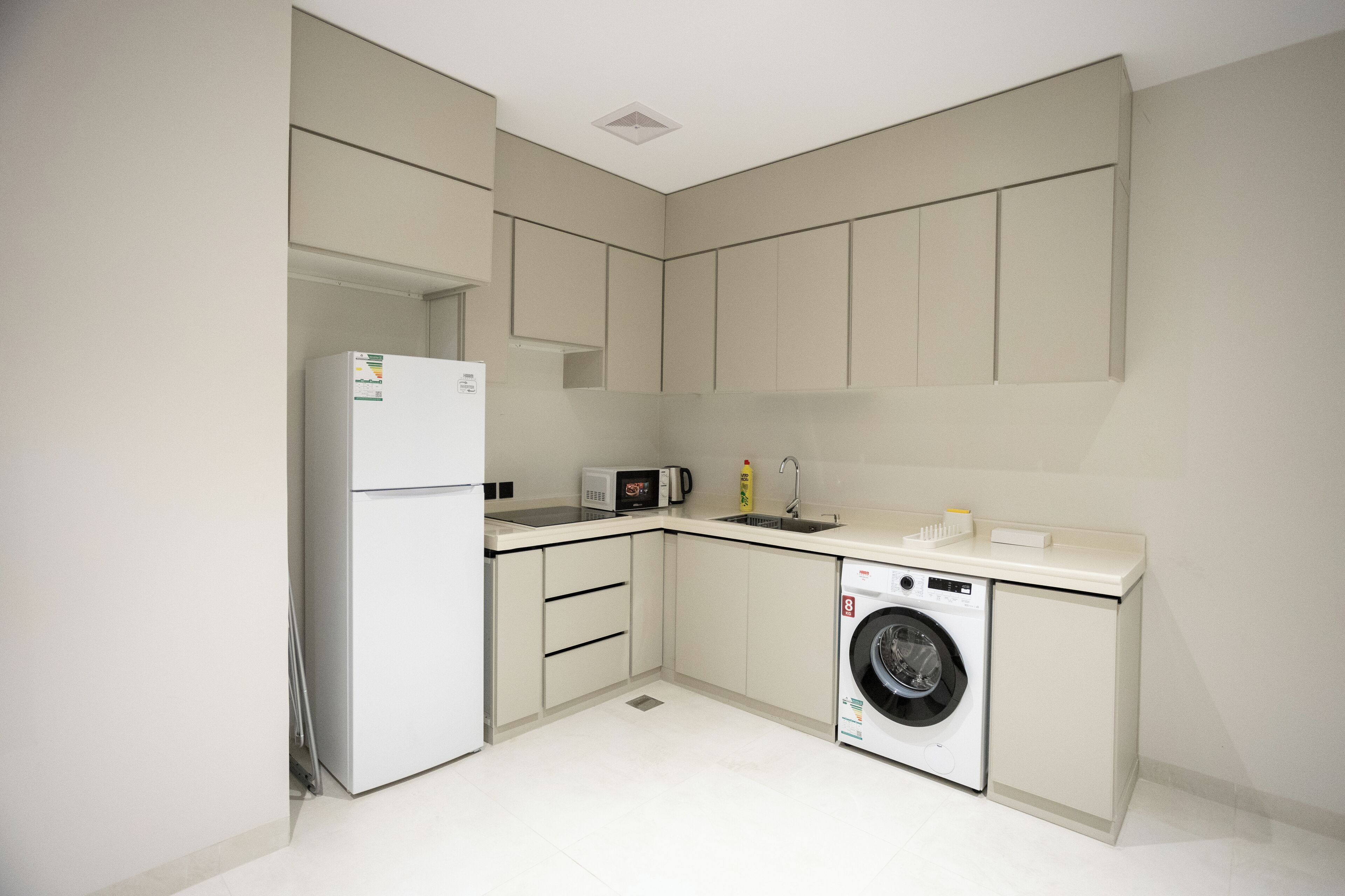A compact kitchen with a refrigerator, microwave, sink, and washing machine.