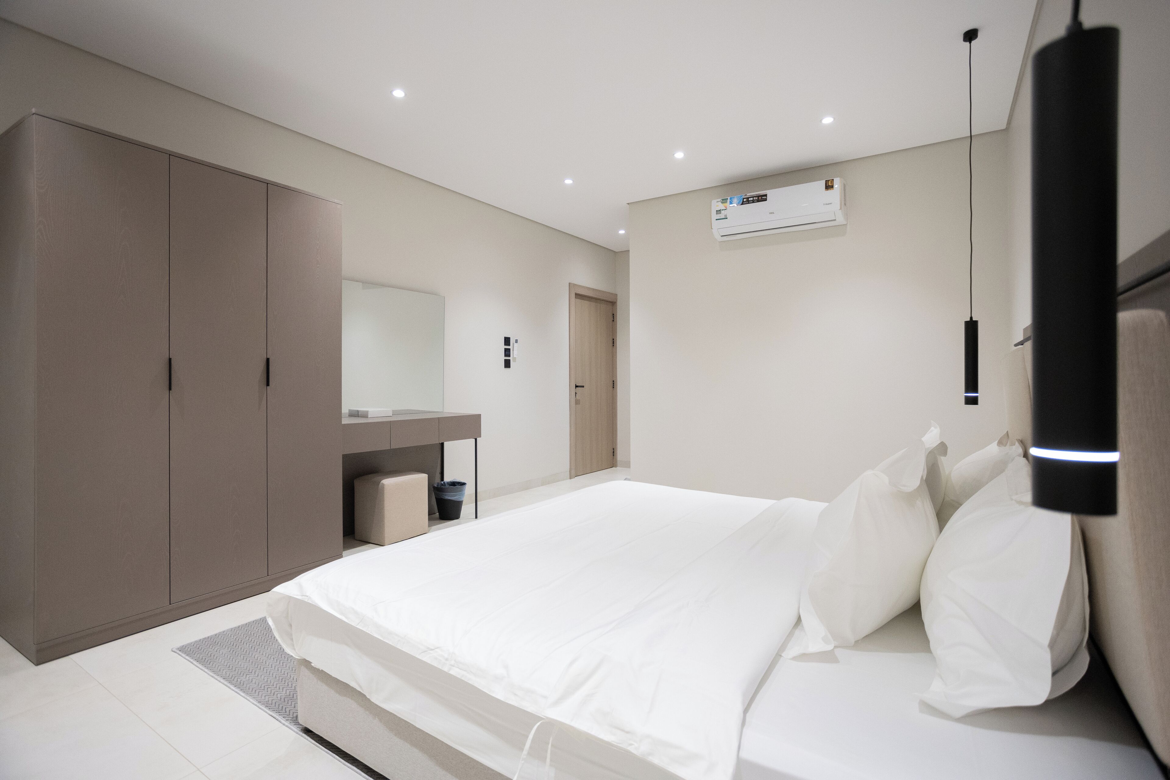 A modern bedroom with a large bed, a wardrobe, a mirror, and an air conditioning unit.