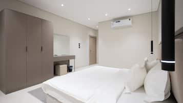 A modern bedroom with a large bed, a wardrobe, a mirror, and an air conditioning unit.