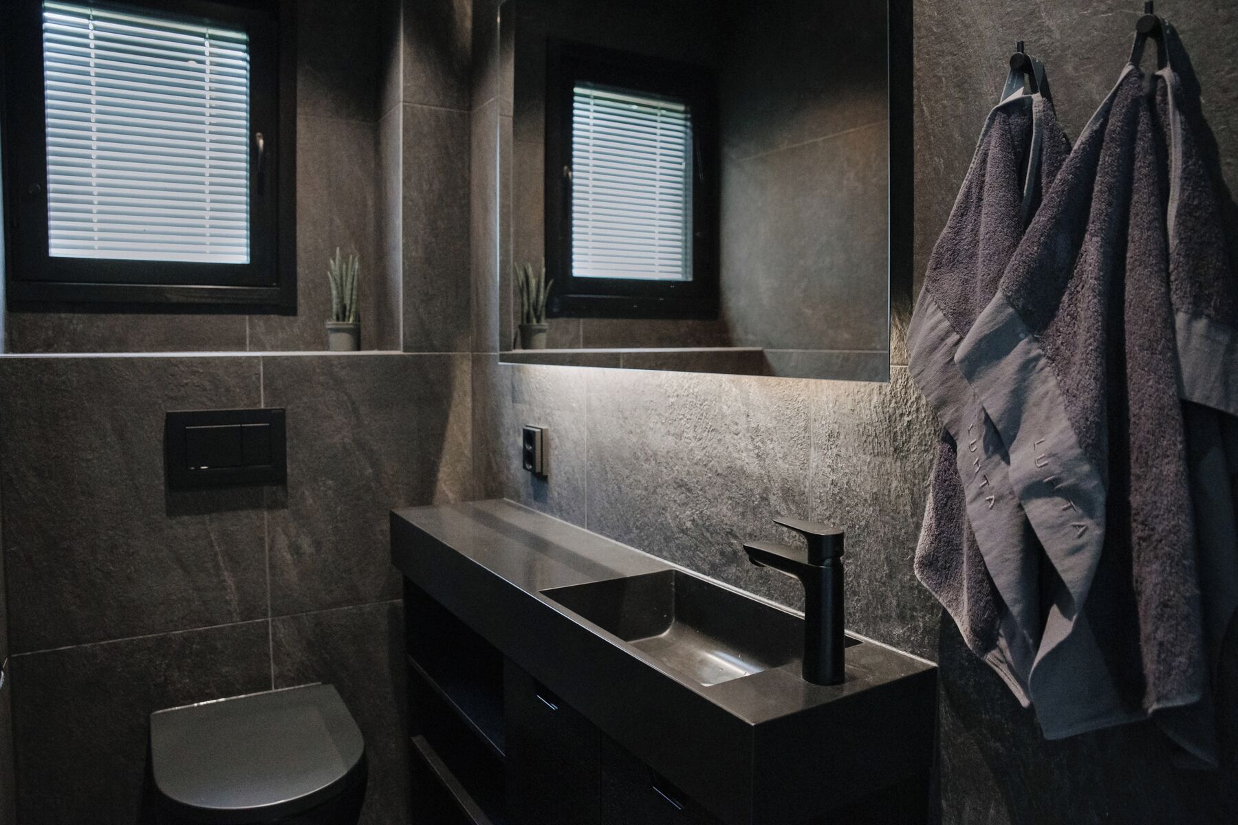 A modern bathroom with a dark-toned sink, a mirror, and a towel rack.