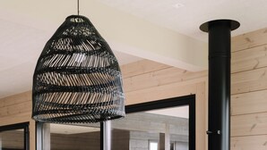 Un salon moderne avec un canapé, un luminaire suspendu noir en fibres tressées et un poêle à bois noir.