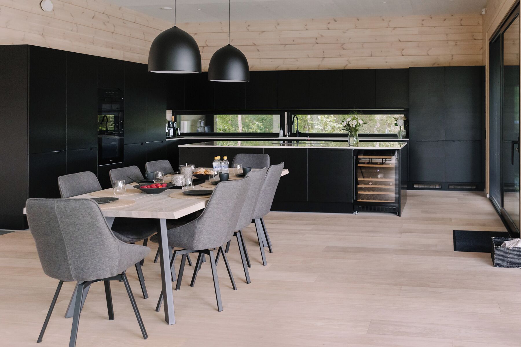 Una cocina moderna con comedor, que incluye una mesa grande con sillas, armarios negros e iluminación colgante.