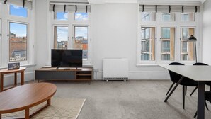 A modern living room with a TV, seating, and large windows.