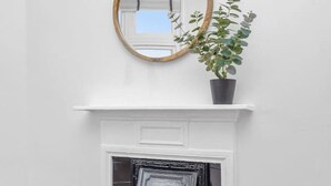 A white fireplace with a black tiled floor, a wooden mantel, and a round mirror above it.