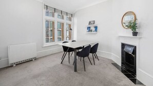 A room with a white radiator, a table with four chairs, a fireplace, and a large window with blinds.