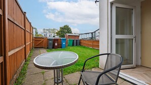 A patio with a round table and two chairs, a wooden fence, and a view of neighboring houses.
