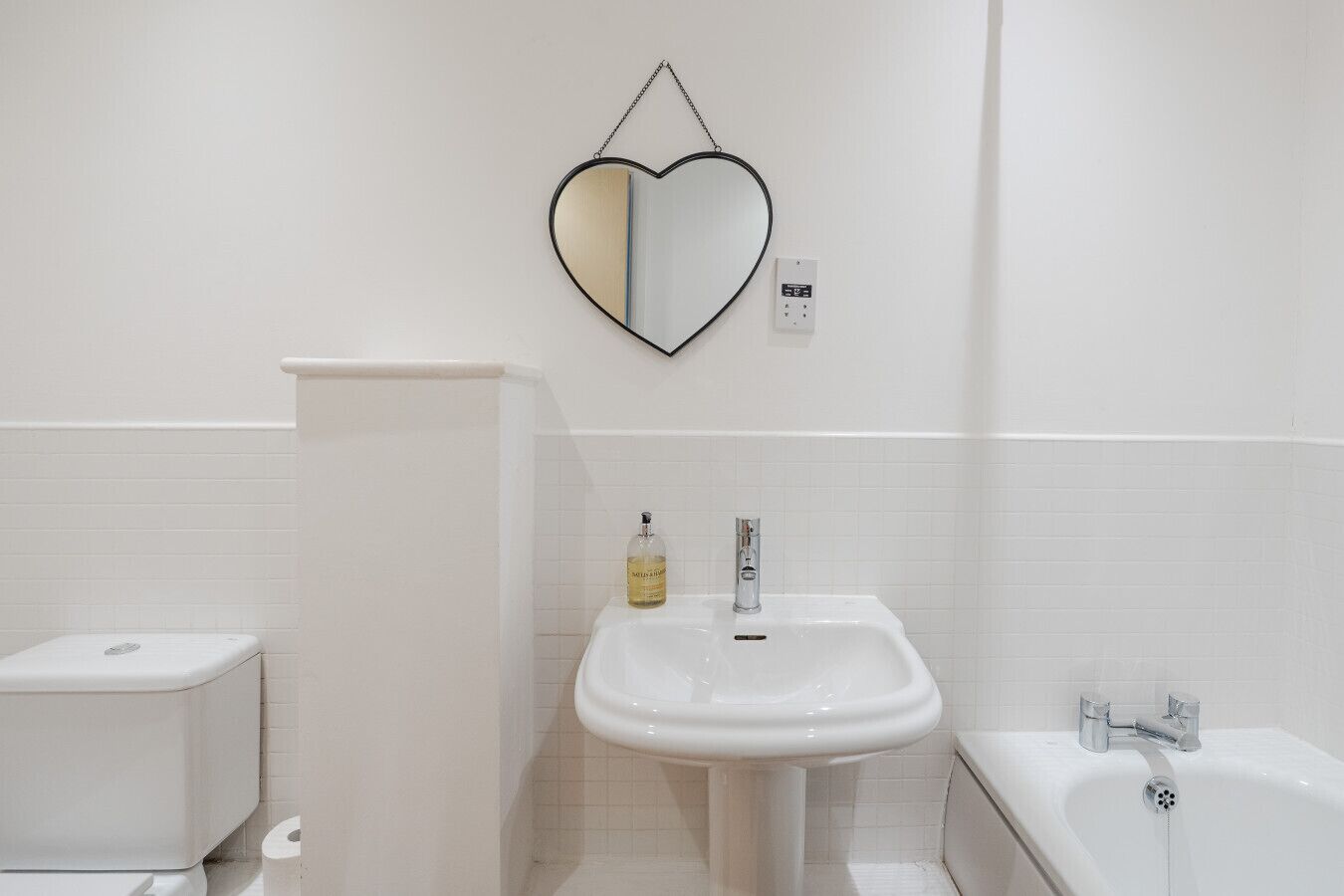 Une salle de bain avec des toilettes blanches, un lavabo sur colonne et une baignoire.