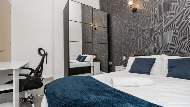 A modern bedroom with a large bed, a desk, and a chair.