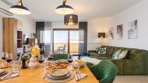 A modern dining area with a wooden table set for a meal, a green sofa, and pendant lighting. - Double D Modern Family Apartment Near Koper (Koper)