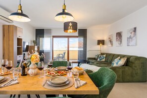 A modern dining area with a wooden table set for a meal, a green sofa, and pendant lighting. - Double D Modern Family Apartment Near Koper (Koper)