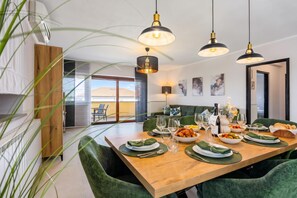 A modern dining area with a wooden table set for a meal, green upholstered chairs, and pendant lighting. - Double D Modern Family Apartment Near Koper (Koper)